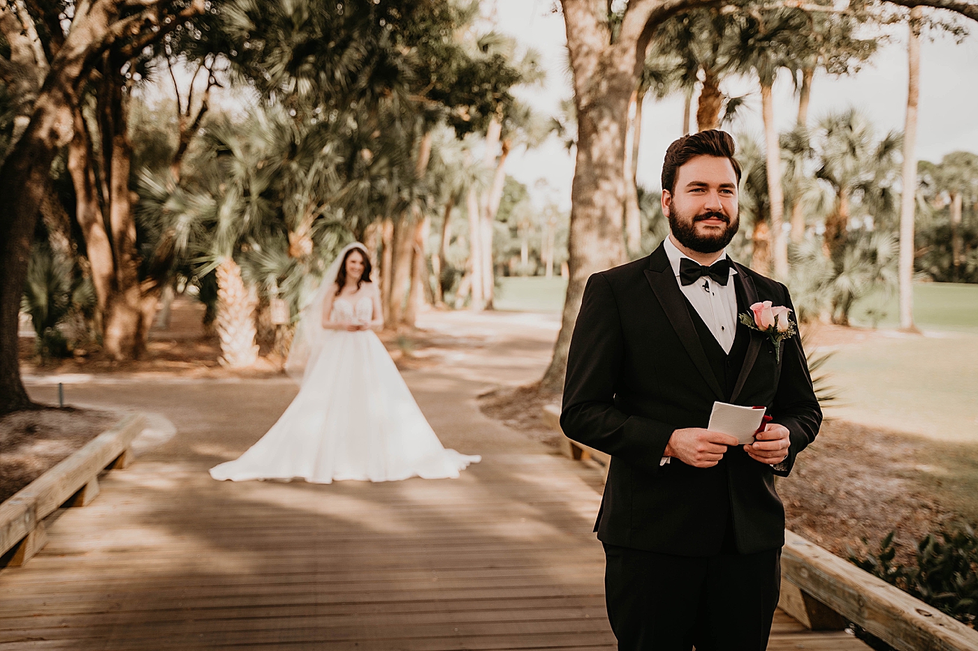 First Look Bride approaching Groom with back turned holding vows on golf course bridge palm trees Romantic Winter Wedding captured NYC Wedding Planner Poppy and Lynn