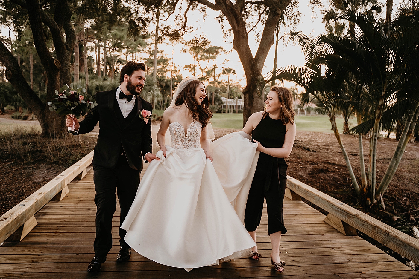 Bride Groom and wedding planner laughing as Groom and Amy Lynn Parmar help Bride by holding wedding dress train with sunset on golf course Romantic Winter Wedding captured NYC Wedding Planner Poppy and Lynn