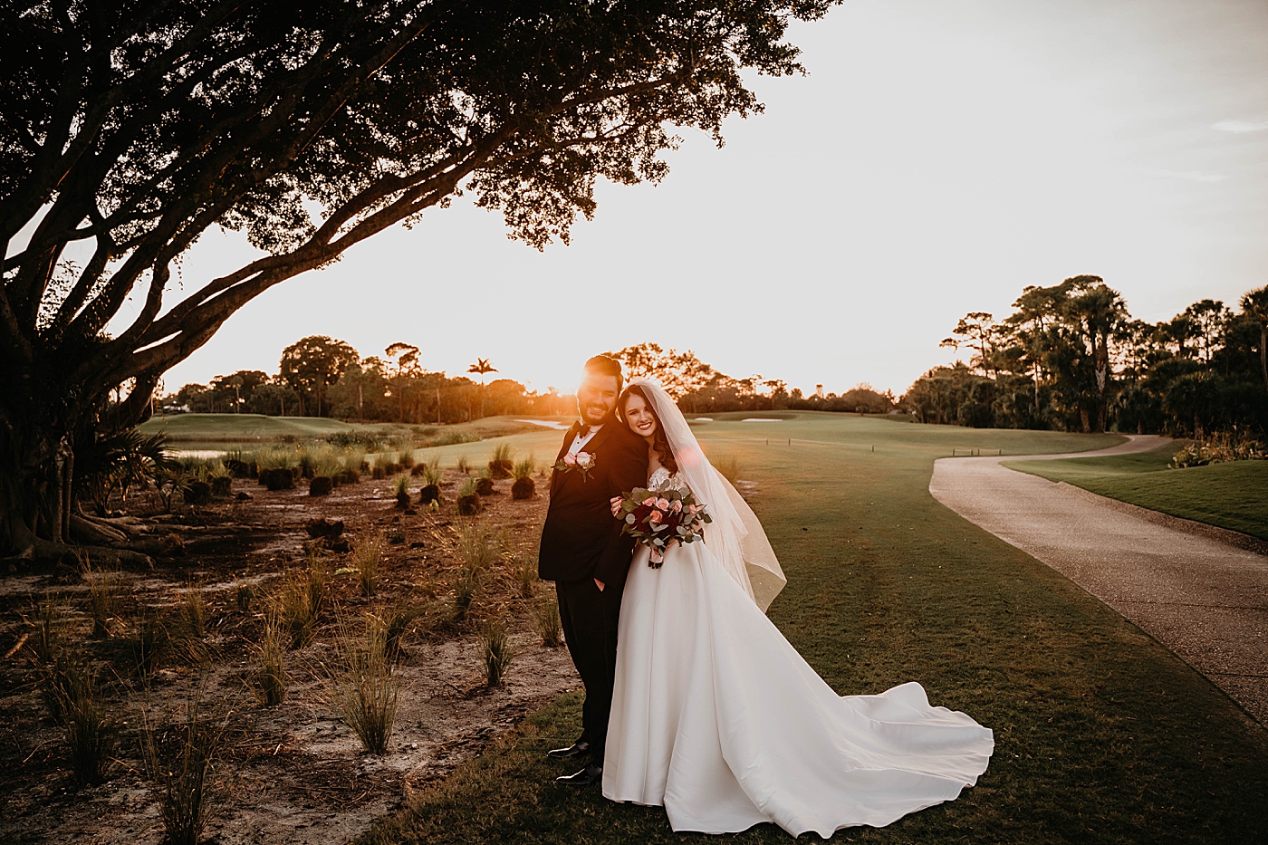 Portrait of Bride resting head on Groom's shoulder on golf fairway with banyan tree and sunset lense flare Romantic Winter Wedding captured NYC Wedding Planner Poppy and Lynn
