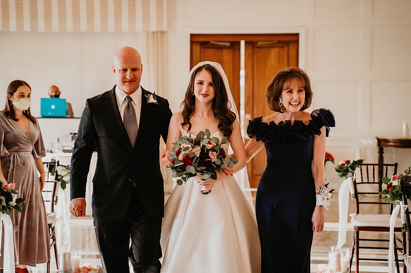 Bride entering ceremony with both parents in arms with red pink white bouquet indoor Romantic Winter Wedding captured NYC Wedding Planner Poppy and Lynn