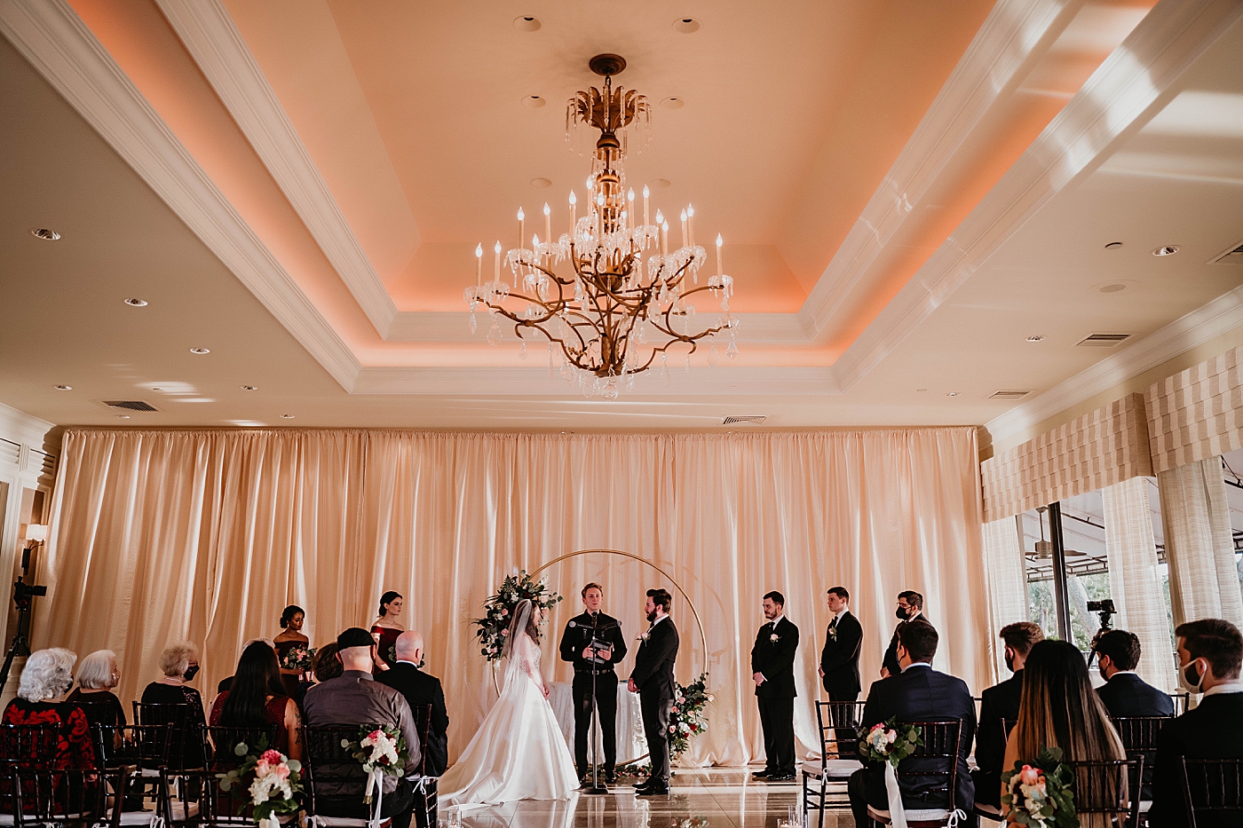 Wide shot of mask on Wedding ceremony homily Bride and Groom looking at each other with vintage chandelier Romantic Winter Wedding captured NYC Wedding Planner Poppy and Lynn