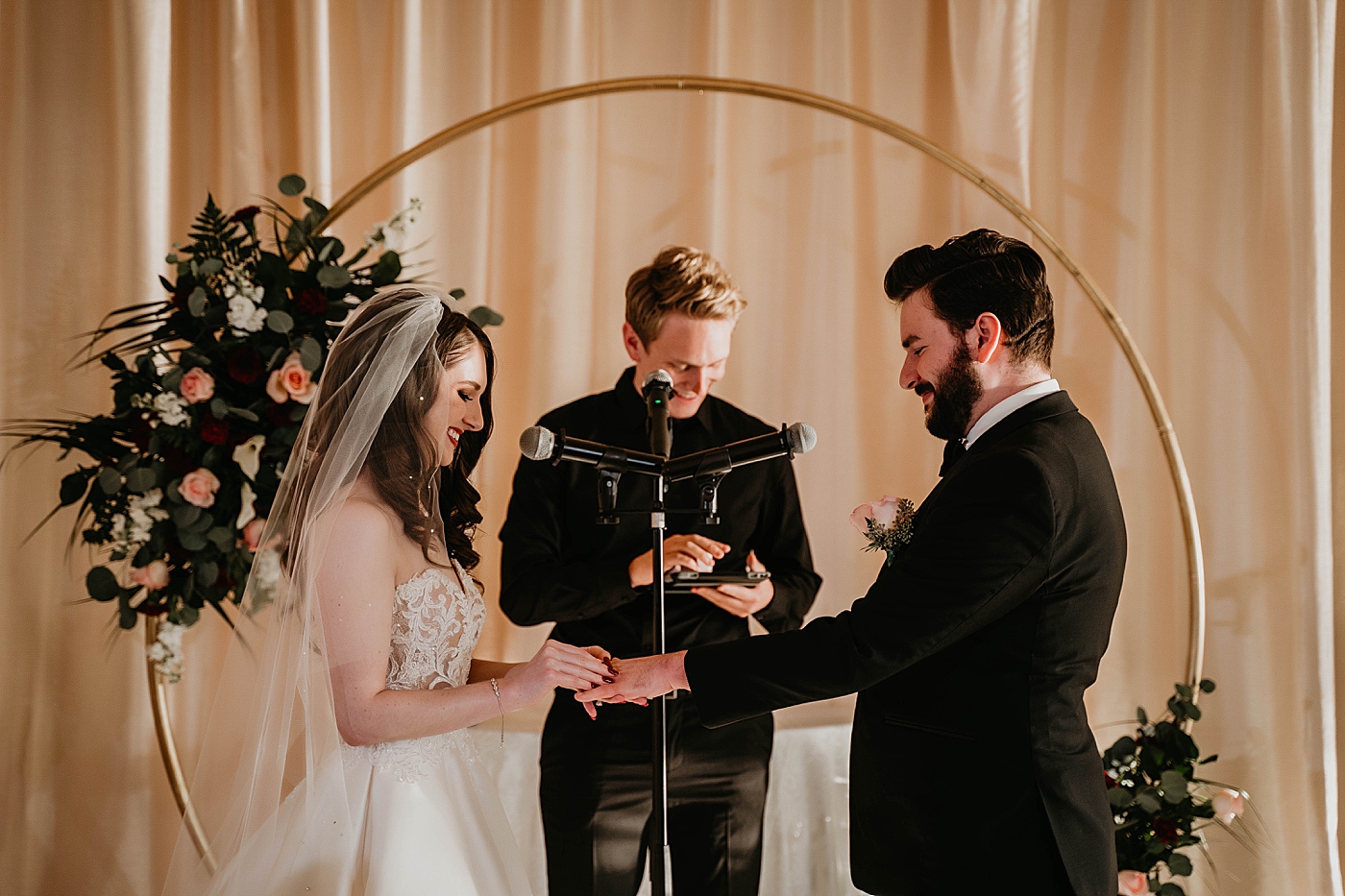 Bride putting ring on Groom with floral decorated gold circular hoop alter piece Romantic Winter Wedding captured NYC Wedding Planner Poppy and Lynn