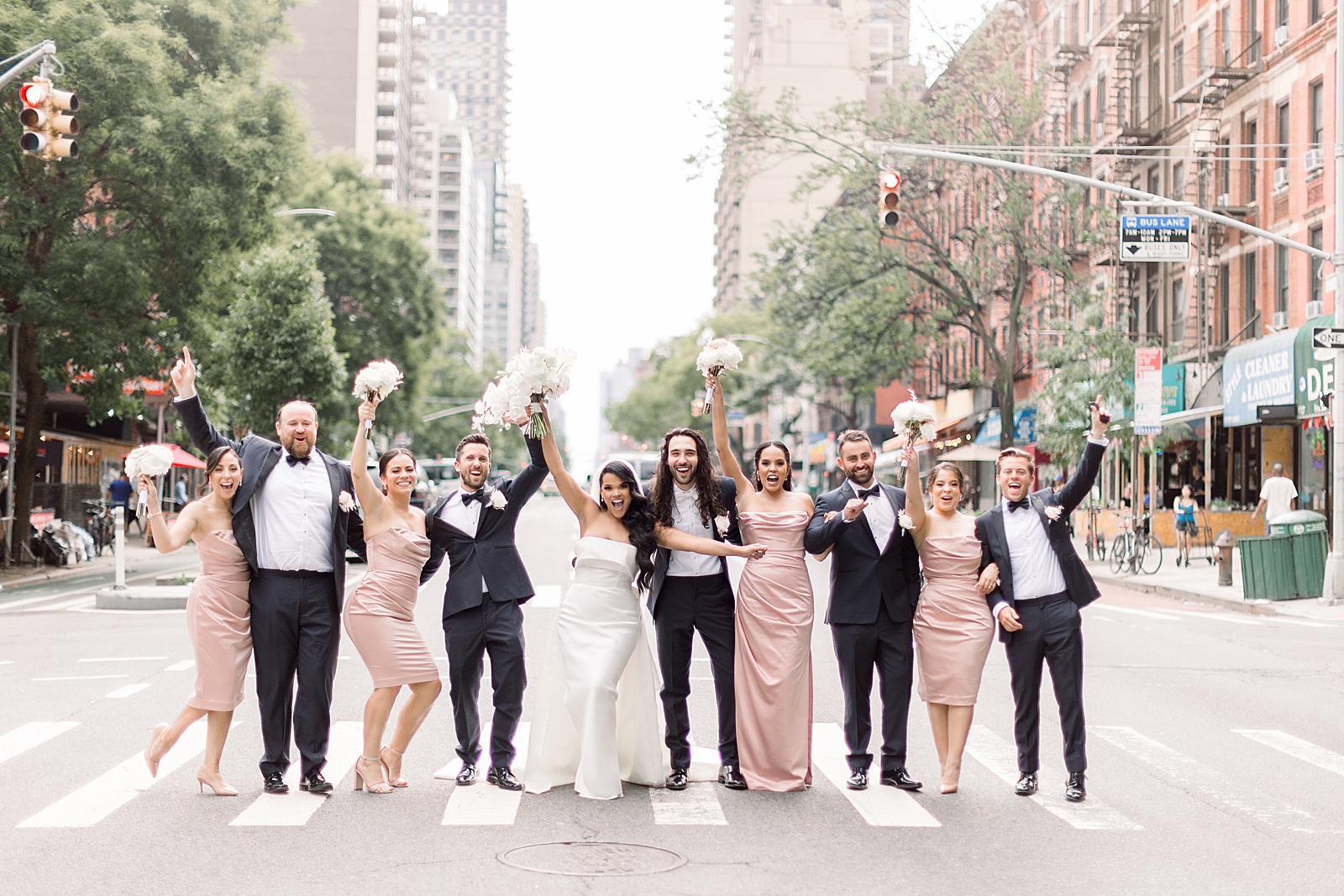 Bride and Groom with wedding party holding up bouquets and hands on New York City cross way