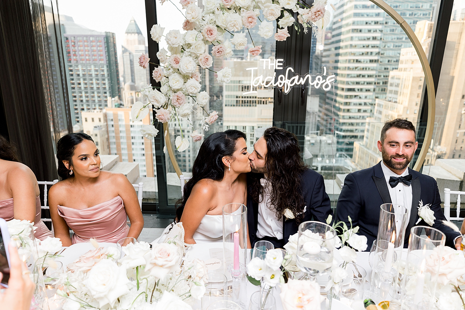 Bride and Groom kissing at wedding party table with Maid of Honor and Best man next to them