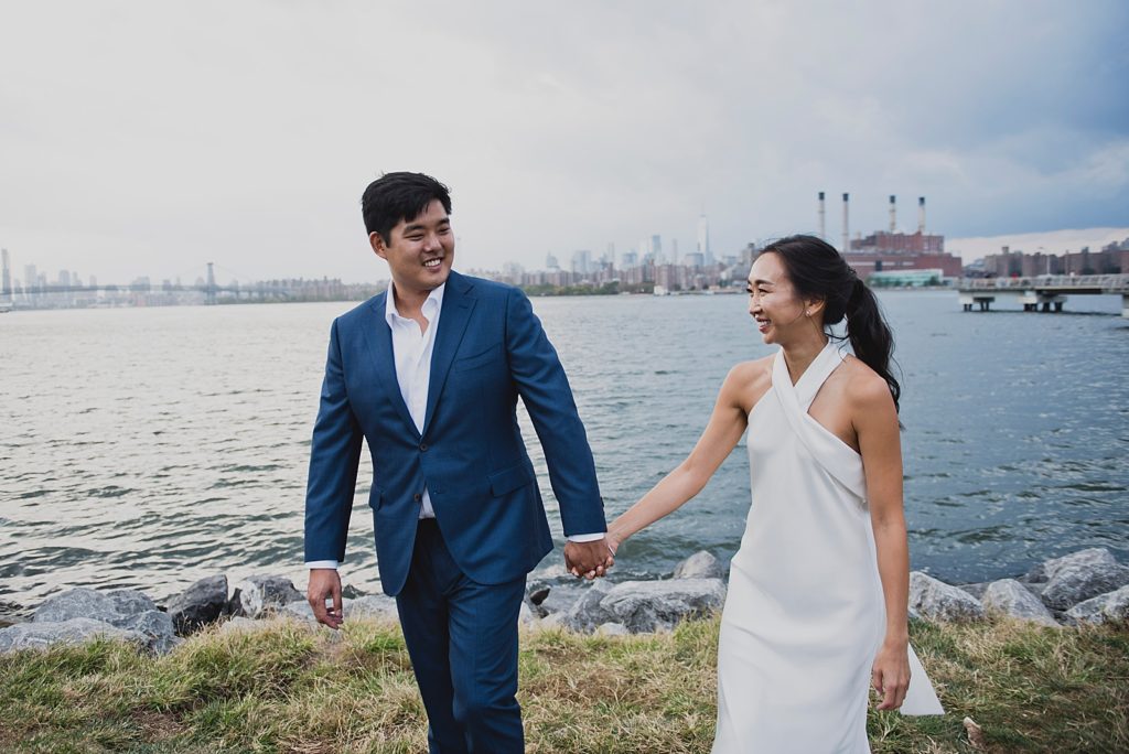 Couple holding hands and walking together on green grass in front of Hudson river