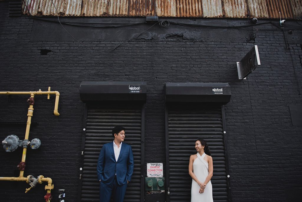 Couple standing in front of garage doors looking at each other by Brooklyn building