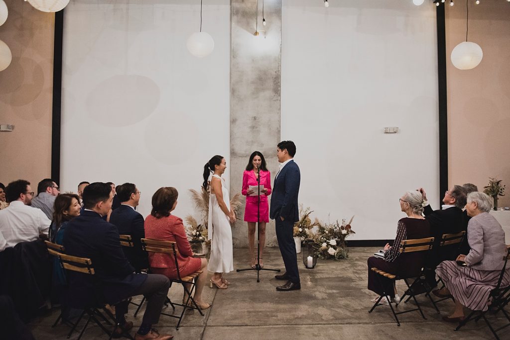 Bride and Groom facing each other for indoor Ceremony with guests watching