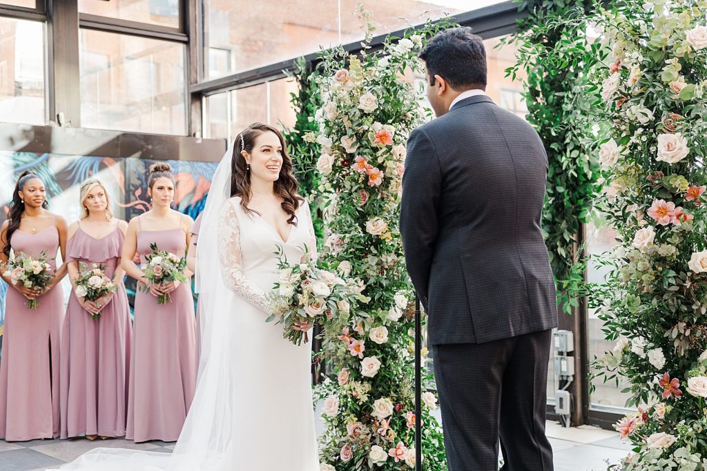 Bride and Groom standing face to face during Ceremony with Bridesmaids in the background