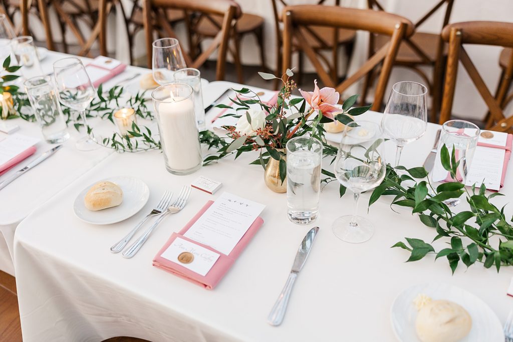 Detail shot of Reception table with white tablecloth pink napkin bread rolls and greenery