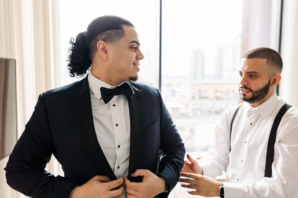 Groom getting ready putting on jacket with help from Groomsman 