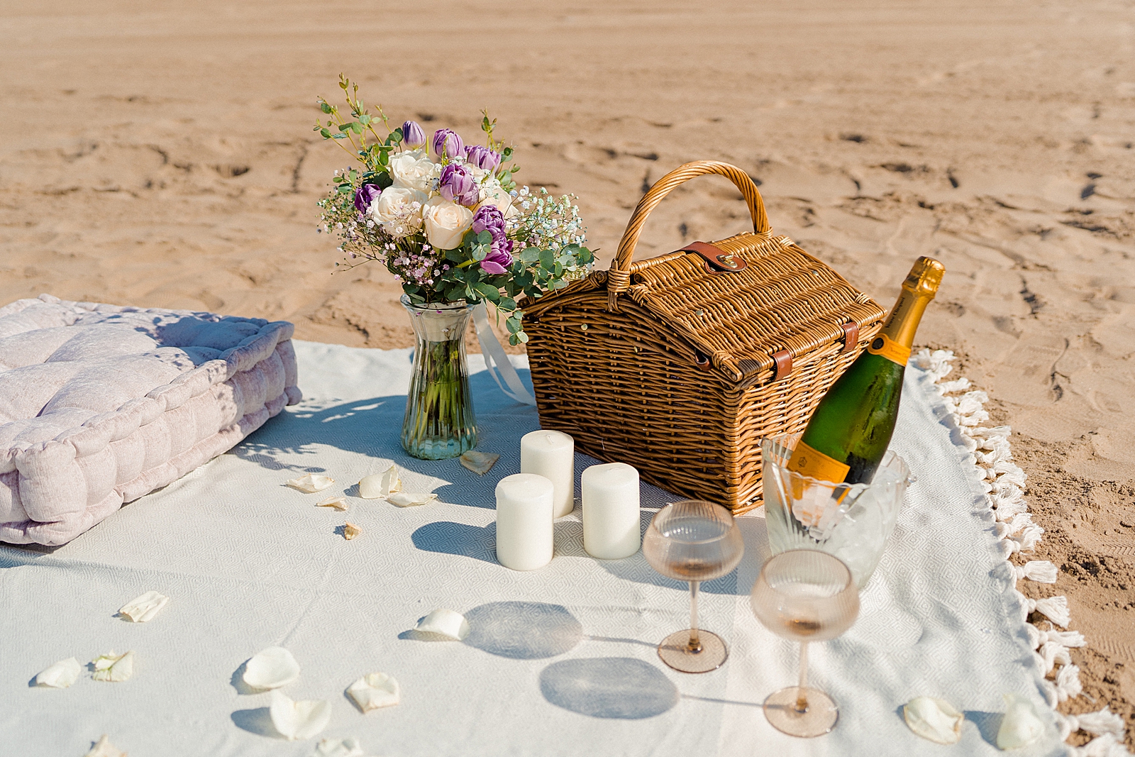 beach picnic proposal set up with picnic basket, veuve clicquot champagne. glasses, and candles