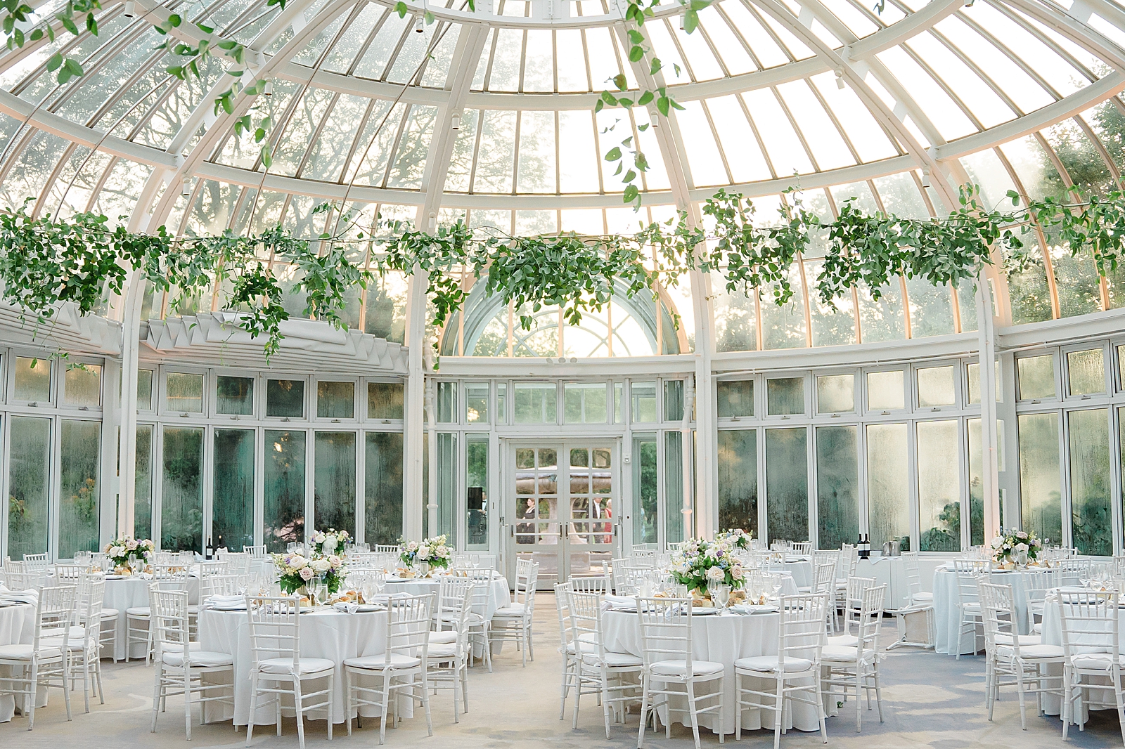 Horizontal shot of the reception space, complete with white table linens, chairs, and greenery draped from the ceiling.