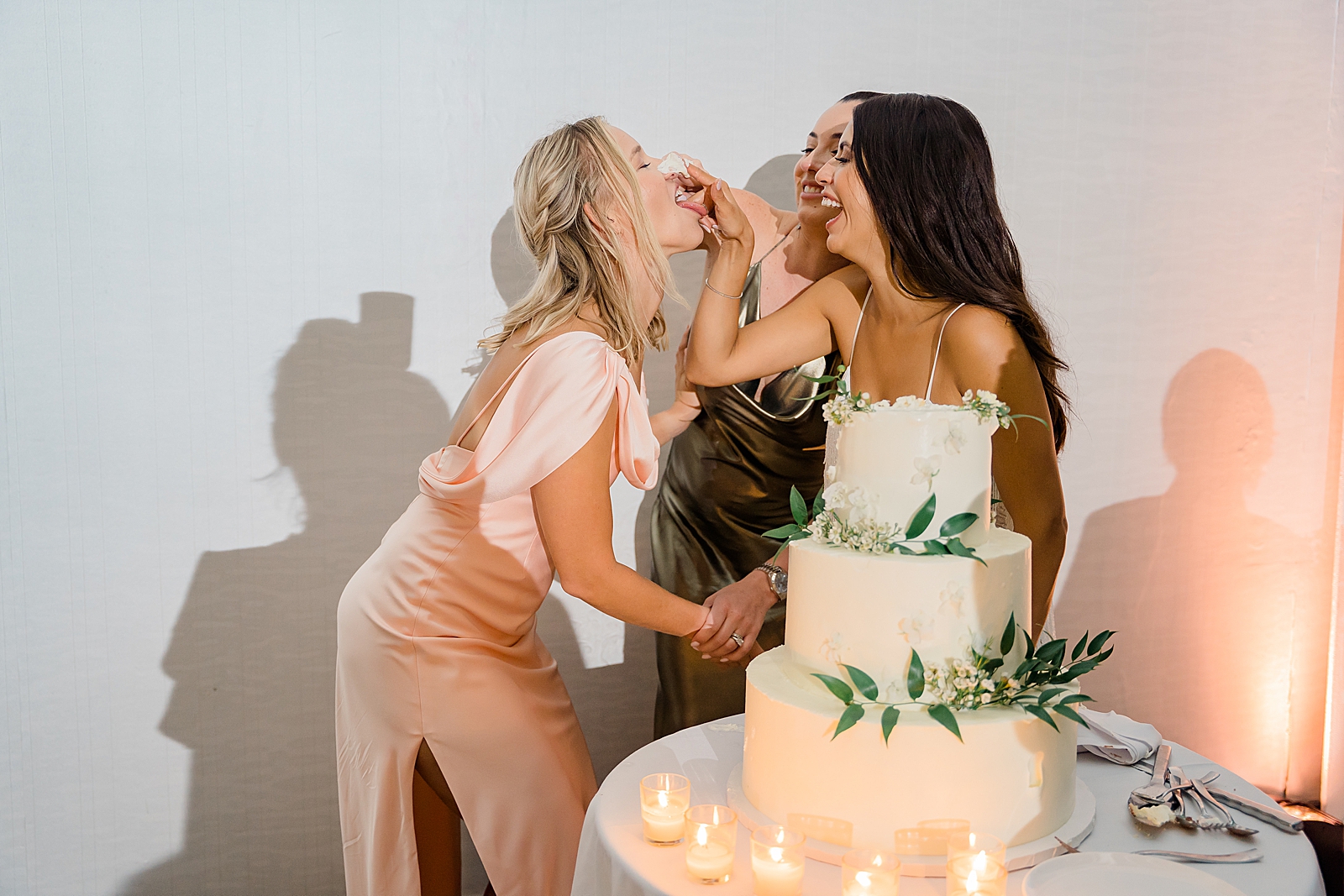 The bride is all smiles as she feeds her bridesmaid cake.