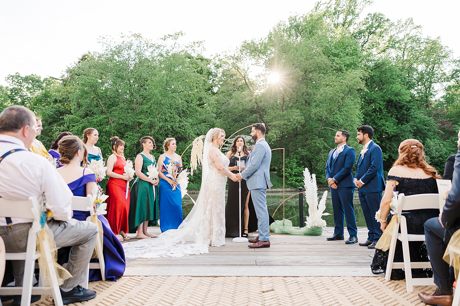 Shot of MK and Eliseo holding hands as they stand at the altar in front of their officiant with their bridesmaids and groomsmen surrounding them. 