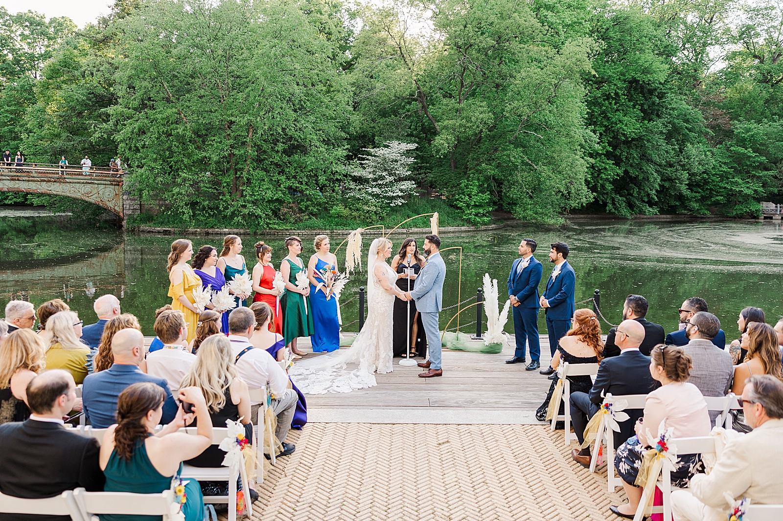 Shot of MK and Eliseo holding hands as they stand at the altar in front of their officiant with their bridesmaids and groomsmen surrounding them, and their guests looking on from their seats. 