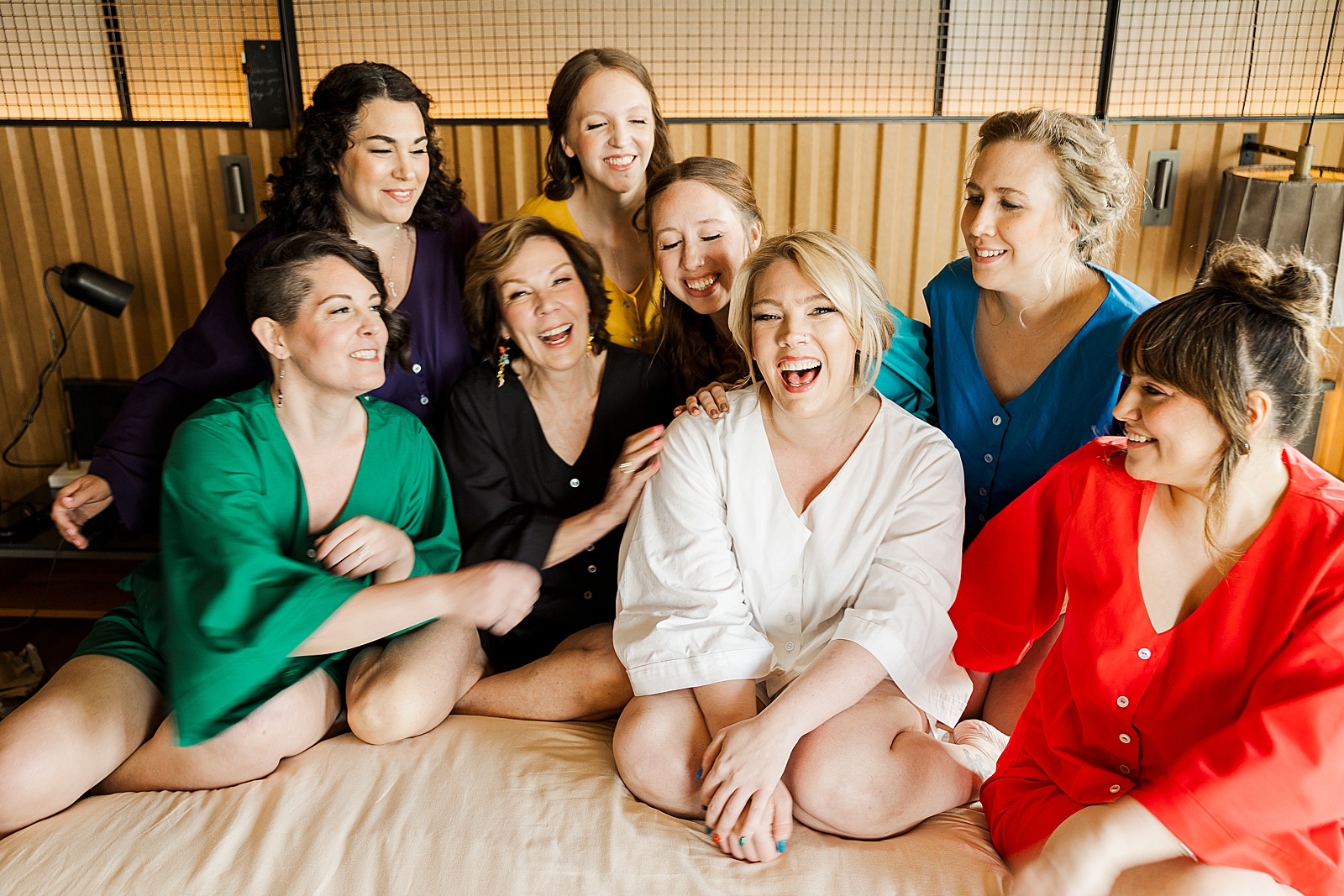 Photo of MK, her mother, and her bridesmaids laughing on top of a bed. 