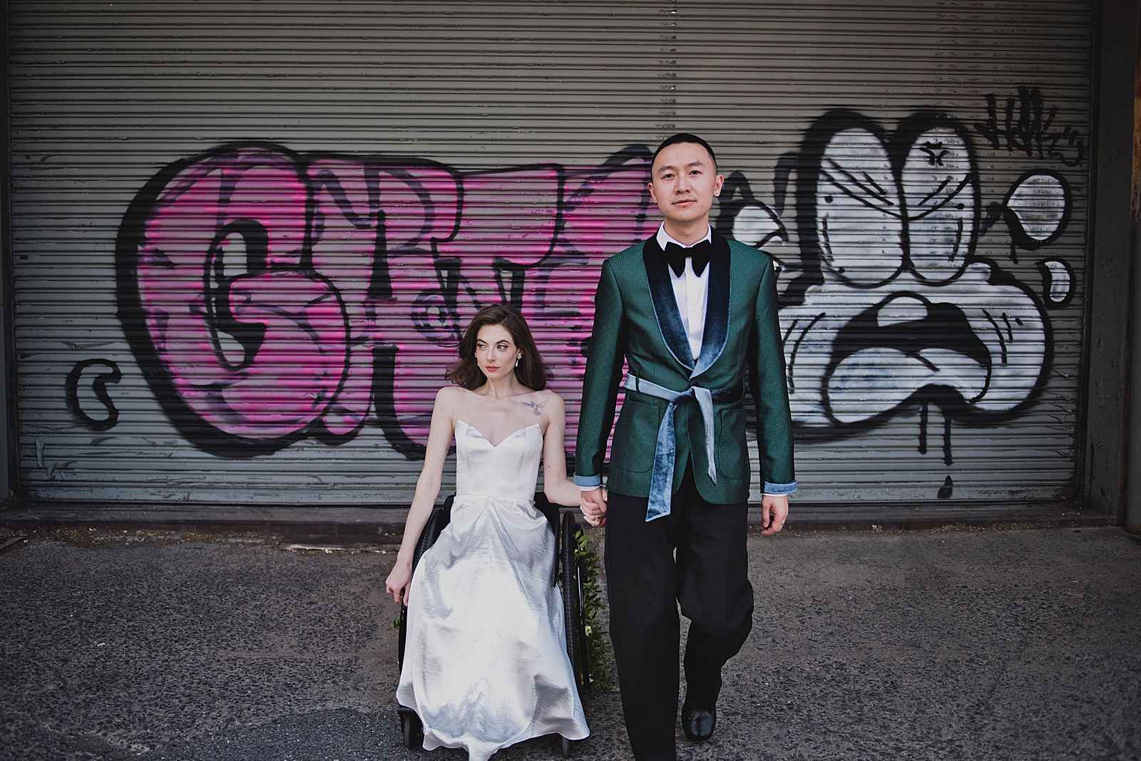 Shot of the bride and groom holding hands in front of a graffiti wall. 