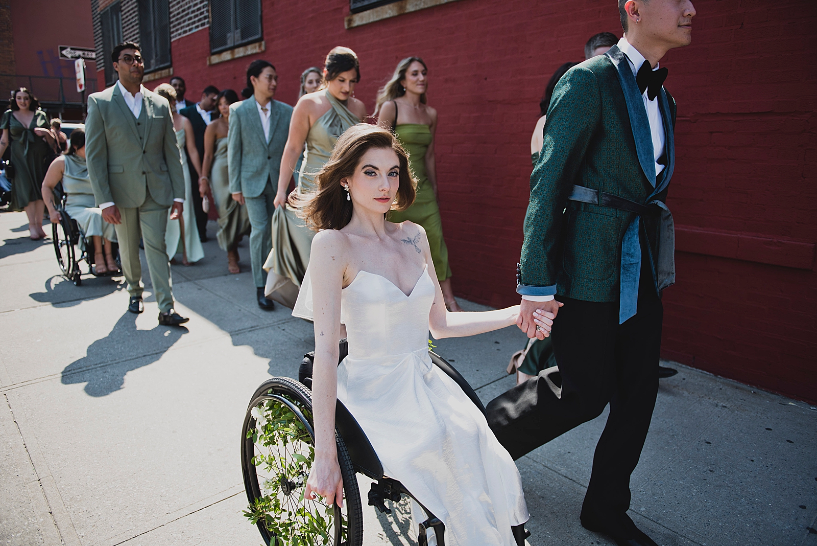 Shot of the bride and groom holding hands as they move down a sidewalk with their bridal party behind them. 