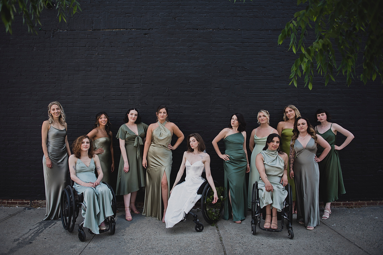 Full shot of the bride posing with her bridesmaids in front of a black brick wall. 