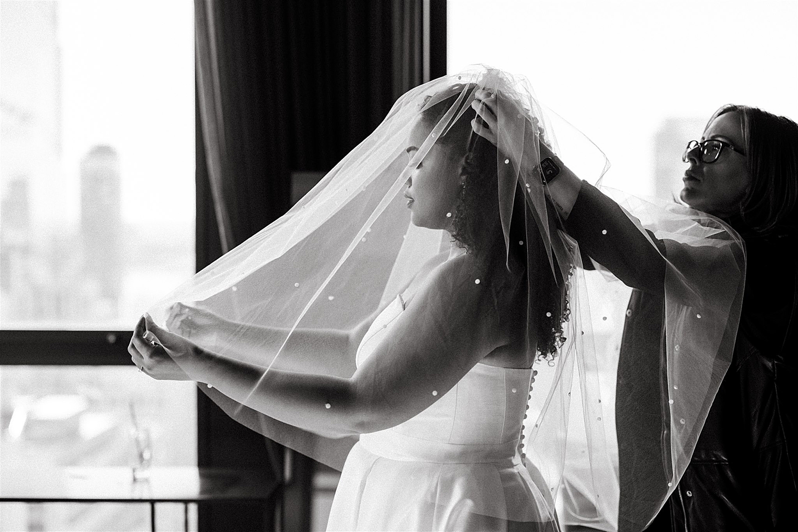 Black and white shot of the bride's hairstylist fastening the veil to the bride's head. 