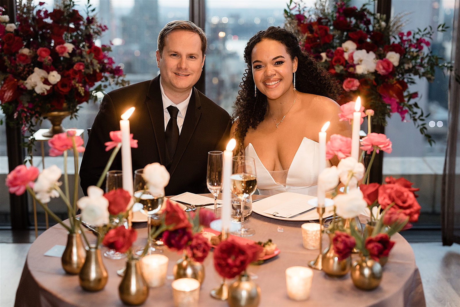 Shot of Bride and Groom smiling for the camera as they sit at their sweetheart table. 