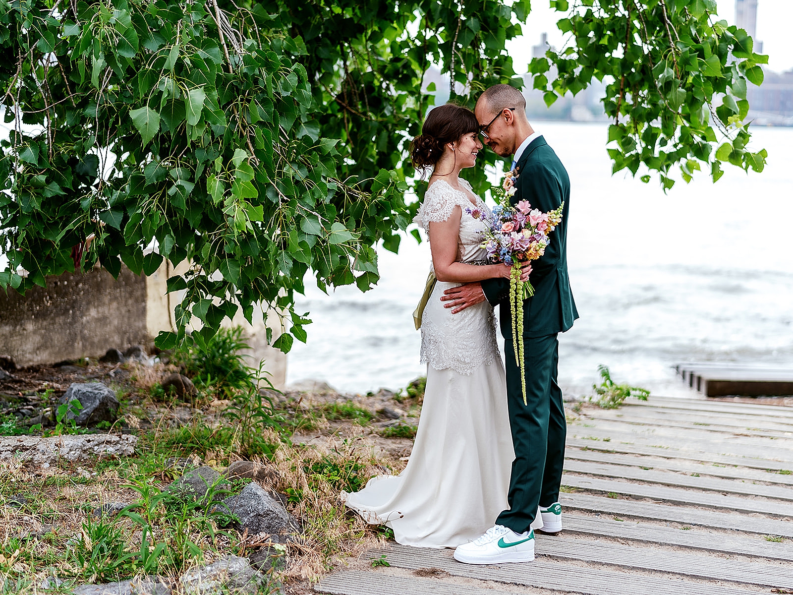 Full body shot of the bride and groom embracing in front of the water. 