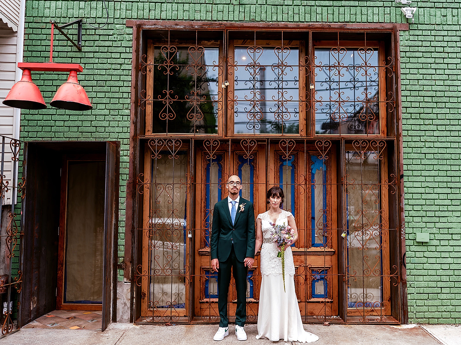 Full body shot of the bride and groom holding hands in front of an old iron gate. 