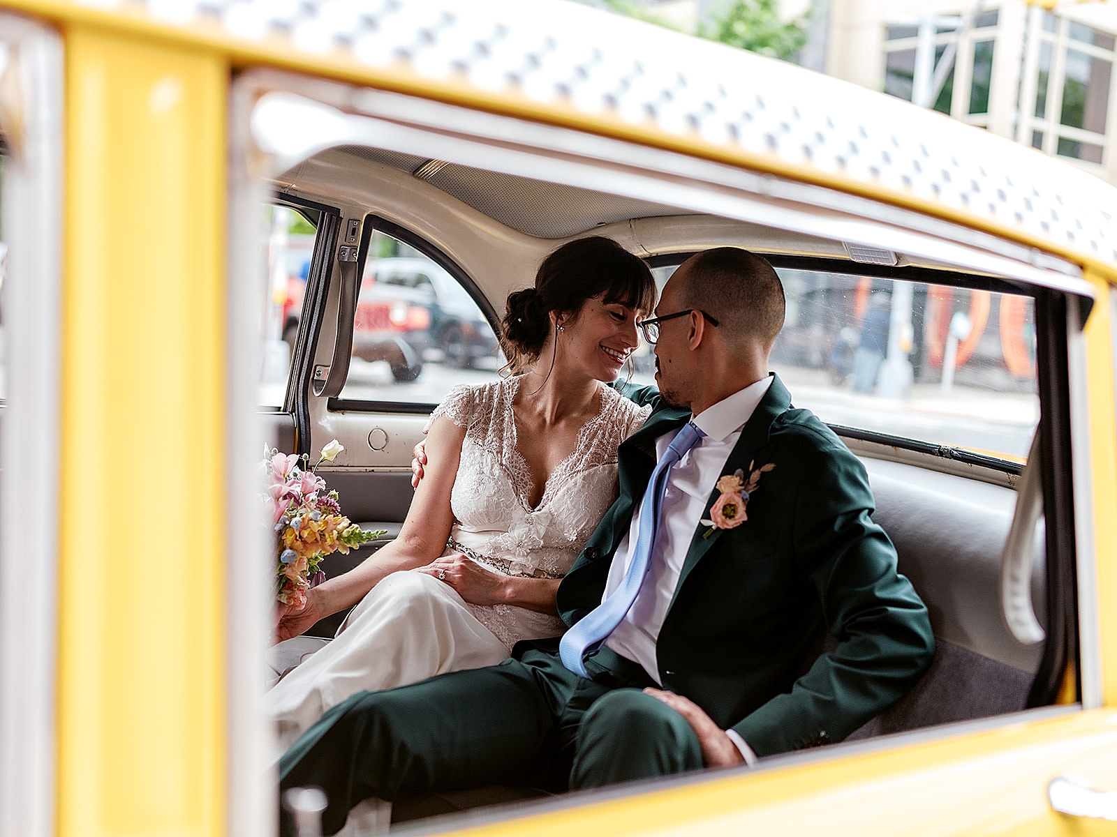 Shot of the bride and groom smiling in the back of a taxi. 