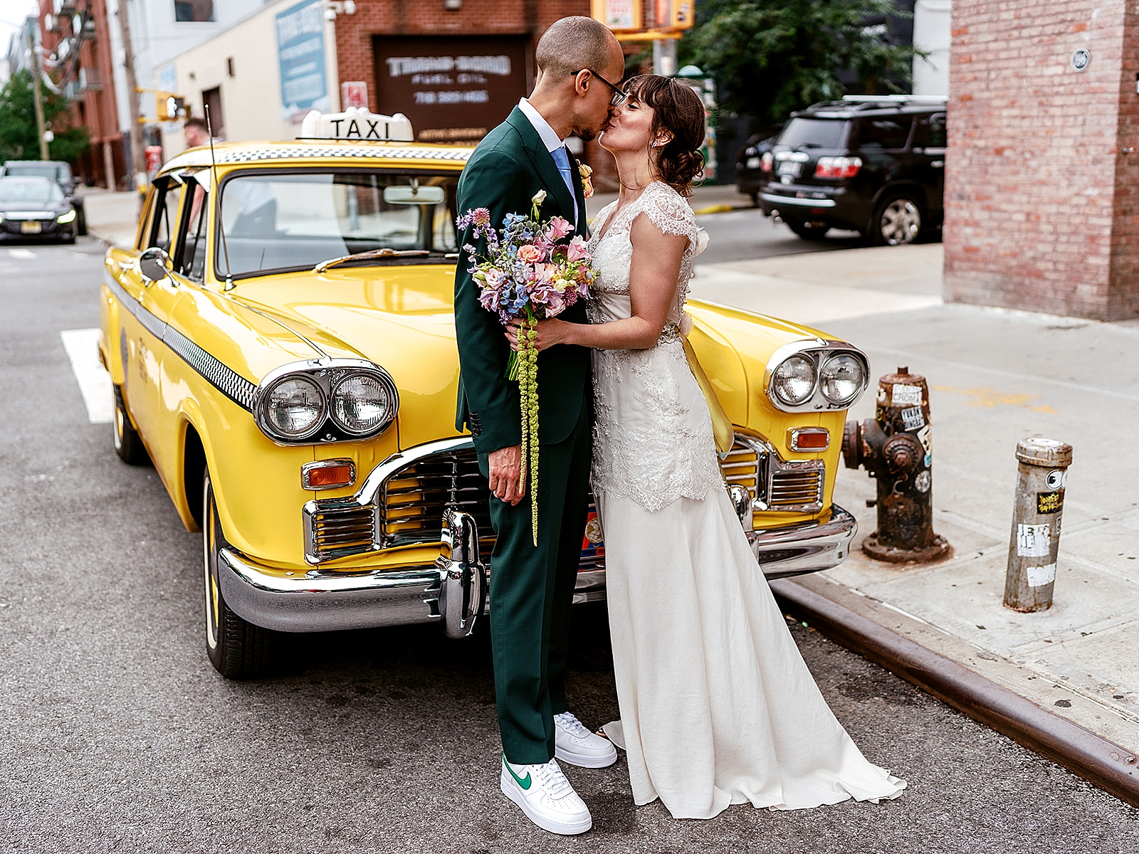 Shot of the bride and groom sharing a kiss in front of an old taxicab. 