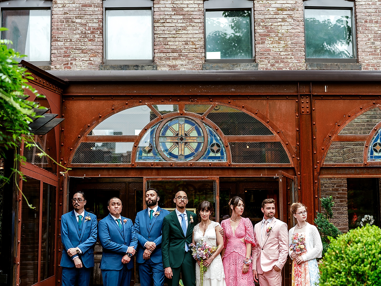 Upper body shot of the bride and groom posing with some of their wedding party in front of the venue. 