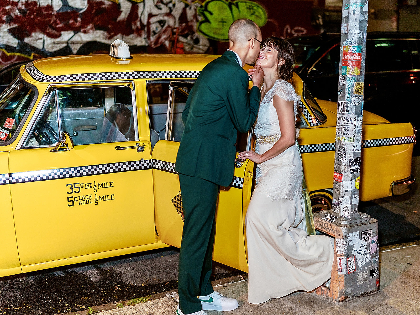 Photo of the bride and groom sharing a kiss in front of a vintage taxicab.