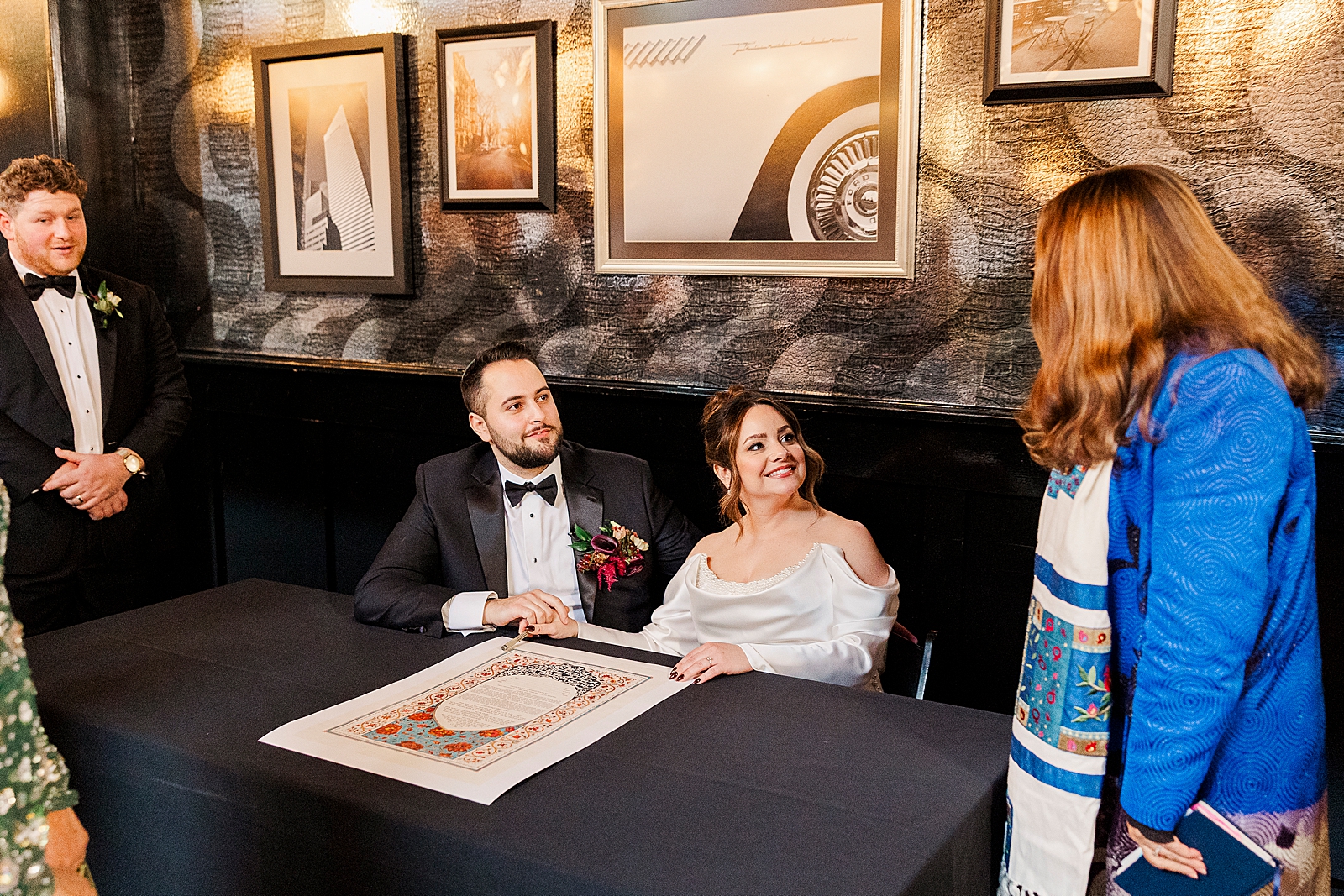 Shot of the bride and groom being all smiles as they sit down to sign the ketubah. 
