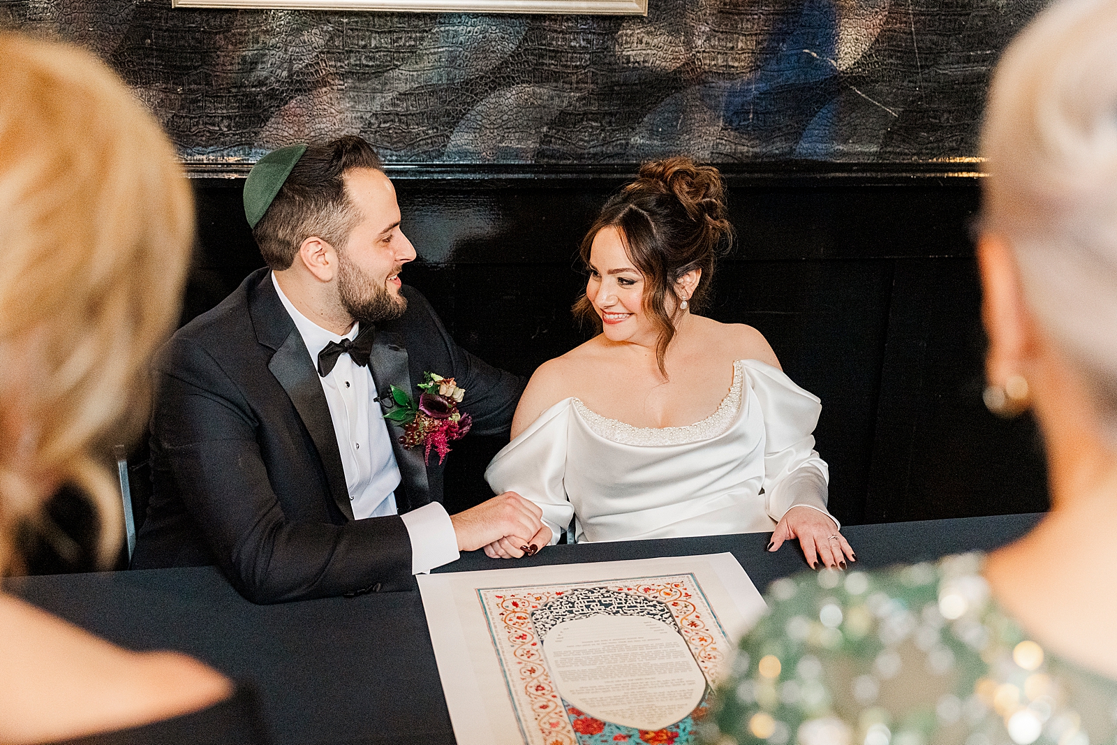 Shot of the bride and groom smiling as they sit down to sign the ketubah. 