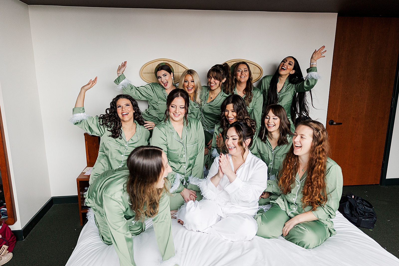 Full shot of the bride and her bridesmaids looking excited on a bed. 