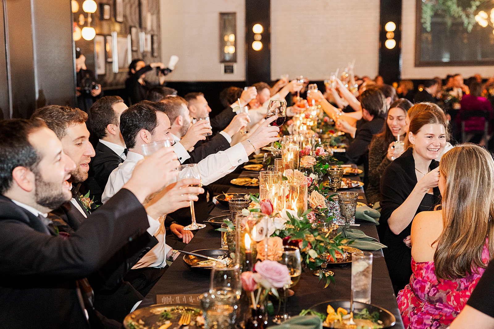 Close up shot of guests at a table lifting their glasses in a toast. 