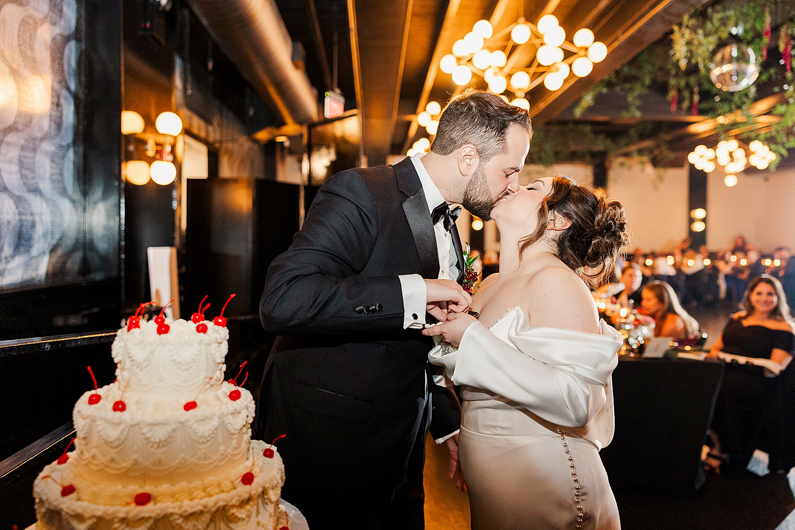 Upper body shot of the couple kissing behind their wedding cake. 