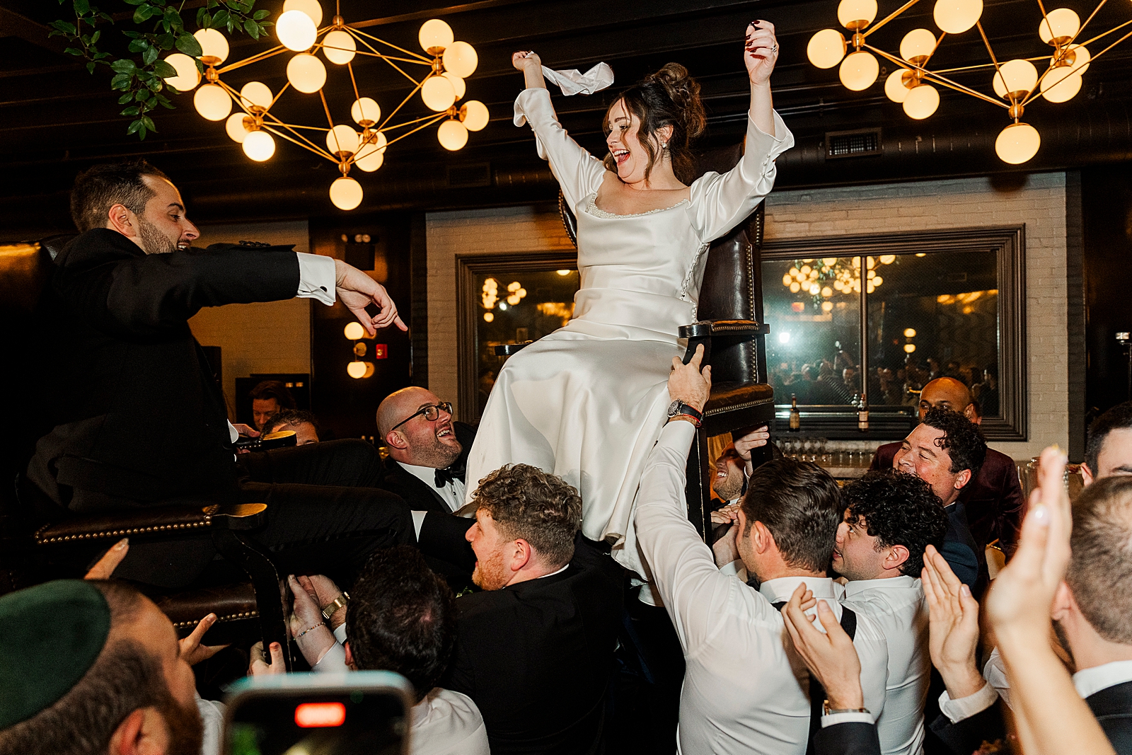 Shot of the Bride and Groom being lifted in chairs by their friends and family during the Hora. 