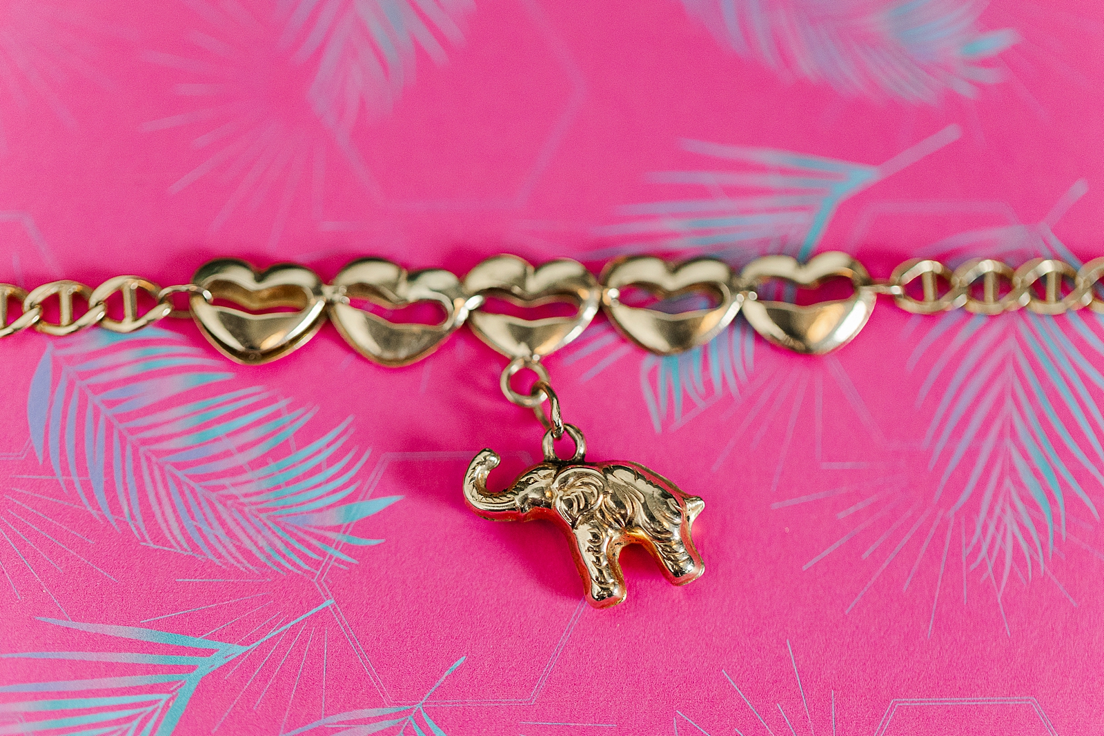 Close up shot of a gold bracelet with hearts on the bangle and an elephant charm. 