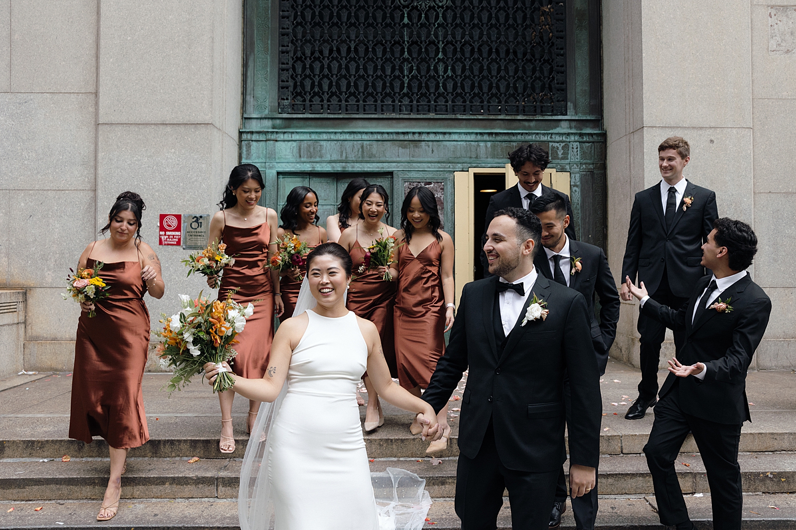 Shot of the couple being all smiles as their bridal party trails behind them.