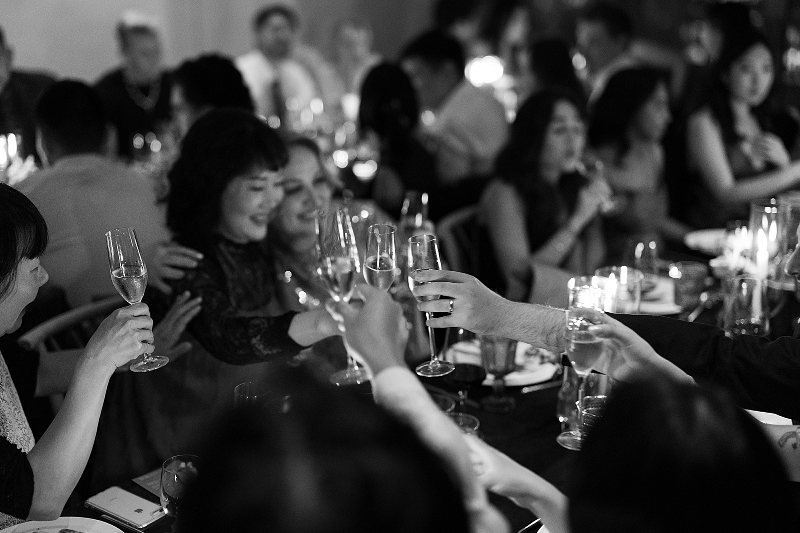 Black and white shot of the wedding guests toasting with their champagne flutes. 