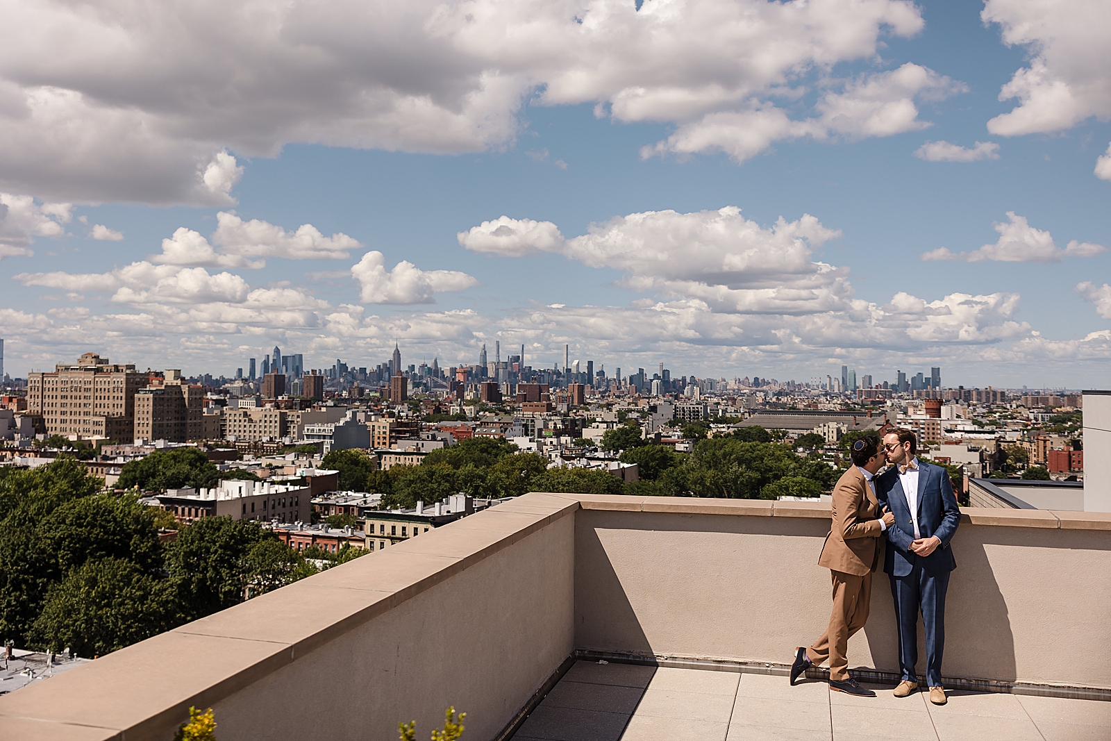 Shot of the grooms sharing a kiss on their Brooklyn rooftop with the Manhattan skyline behind them.